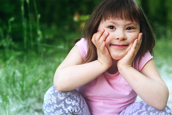 photo of a young girl with downs syndrome crouching and smiling with her hands on her face